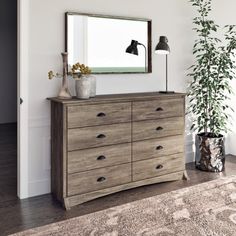 a dresser with a mirror and lamp on top of it next to a potted plant