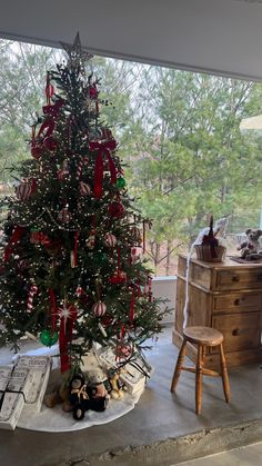 a decorated christmas tree sitting on top of a table next to a chair and window