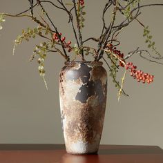 a vase filled with branches and berries on top of a wooden table next to a wall