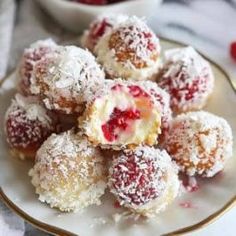 a white plate topped with powdered sugar covered donuts next to a bowl of strawberries