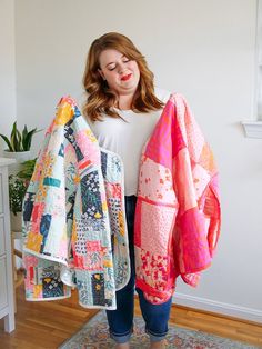 a woman standing in front of a white wall holding two colorful quilts