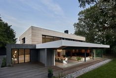 a modern house with wooden decking and white furniture on the outside, surrounded by trees