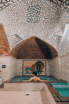 a woman is sitting in the middle of a swimming pool with tiled walls and ceiling