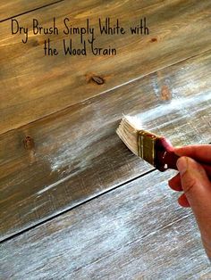 a hand holding a paintbrush over a wood grain surface with the words dry brush simply white with the wood grain