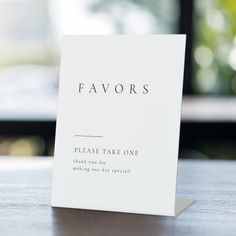 a white card with the words favors on it sitting on a table next to a window