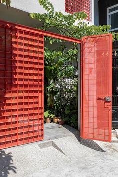 two red doors are open in front of a house with plants and potted trees