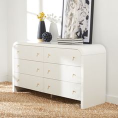 a white dresser with two vases on top of it and a painting hanging above