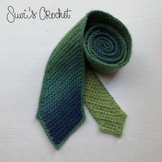 a green and blue knitted tie sitting on top of a white table next to the words sujo's crochet