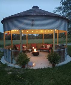 an outdoor fire pit in the middle of a grassy area with chairs and lights on it