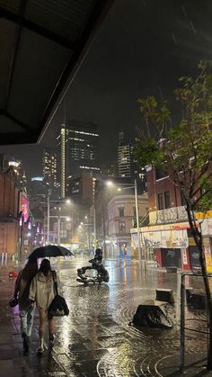 people walking in the rain with umbrellas on a city street at night near buildings