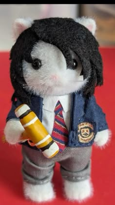 a small stuffed animal wearing a suit and tie holding a yellow object in its hand