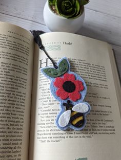 an open book with a felt flower and bee decoration on it, next to a potted plant