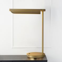 a gold desk lamp sitting on top of a black table next to a white wall