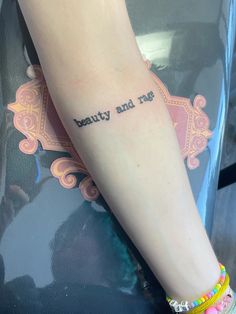 a woman with a tattoo on her arm that says beauty and the beast in cursive writing