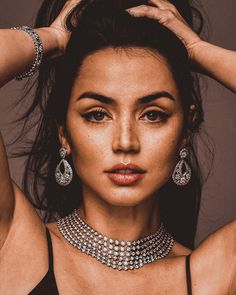 an image of a woman with jewelry on her neck and hands behind her head, looking at the camera