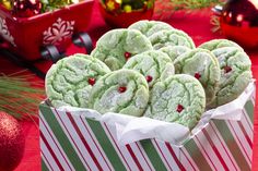 a box filled with green and white cookies on top of a red table next to christmas decorations