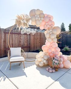 an arch made out of balloons is in the middle of a backyard with a chair and table