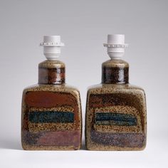 two brown and black bottles sitting next to each other on top of a white surface