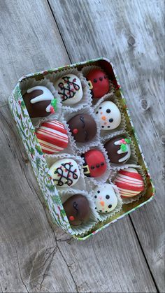 a box filled with assorted decorated chocolates on top of a wooden table next to a cupcake