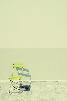 a green chair sitting on top of a stone floor next to a wall and water