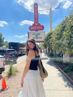 a woman standing on the sidewalk in front of a motel sign with cars parked nearby