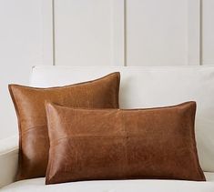 two brown leather pillows sitting on top of a white couch