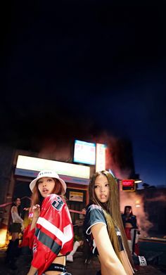 two young women standing next to each other in front of a building with neon lights