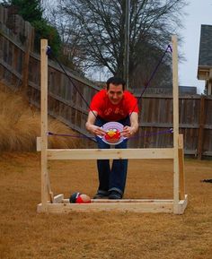 a man holding a frisbee on top of a wooden structure in a yard