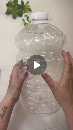 a person holding a large plastic water bottle on top of a white table next to a plant