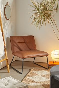 a brown chair sitting in front of a plant next to a lamp and rug on the floor