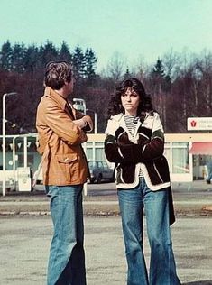 two people standing in the middle of a parking lot with trees in the back ground