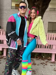 a man and woman dressed in colorful clothing posing for a photo on a pink bench