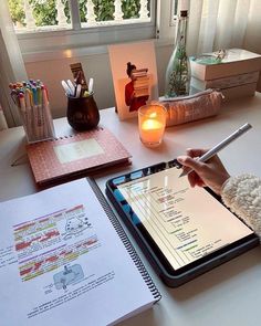 a person sitting at a desk writing on a tablet with a pen and notebook in front of them