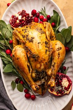 a roasted turkey on a white platter surrounded by cranberries and pomegranates