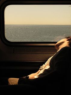 a person sitting on a train looking out the window at the water and land below