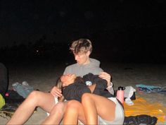 two people are laying on the beach at night, one is kissing the other's head