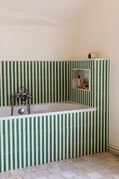 a bathroom with green and white striped tiles on the walls, bathtub and sink