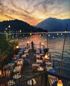 an outdoor dining area with lanterns lit up on the water at sunset or dawn,