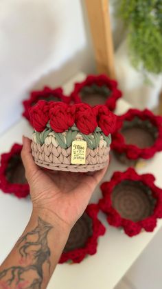 a hand holding a small crocheted basket with red flowers on it, in front of several smaller crocheted baskets