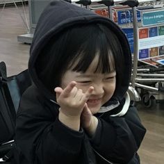 a young child sitting in an airport holding his hand up to his face and smiling at the camera