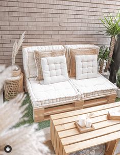 a white couch sitting on top of a wooden table next to a green plant in front of a brick wall