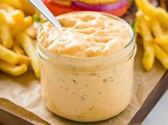 a sandwich and french fries on a wooden tray with a jar of sauce next to it