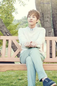 a young man sitting on a wooden bench in the park with his hands clasped to his knees