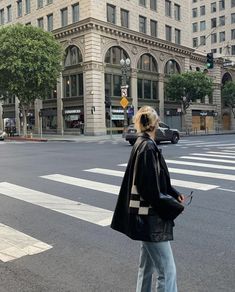 a woman standing at an intersection in front of a large building