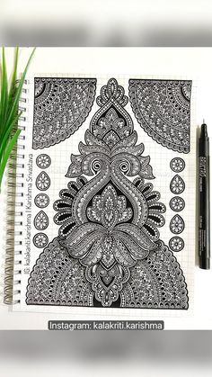 a notebook with an intricate design on it next to a pen and some green plants