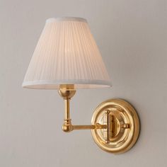 a wall light with a white shade on it's side and a gold arm