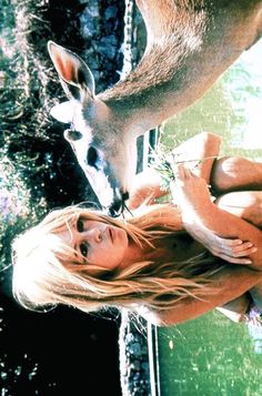 a woman standing next to a deer near a body of water