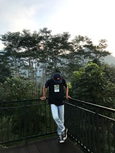 a man standing on top of a wooden deck next to a lush green forest filled with trees