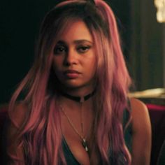 a woman with long pink hair sitting in a chair and looking at the camera while wearing a choker necklace