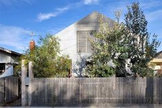 a white house with a wooden fence in front of it and trees on the other side